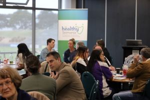 People talking with each other with the Healthy Tasmania banner in background.