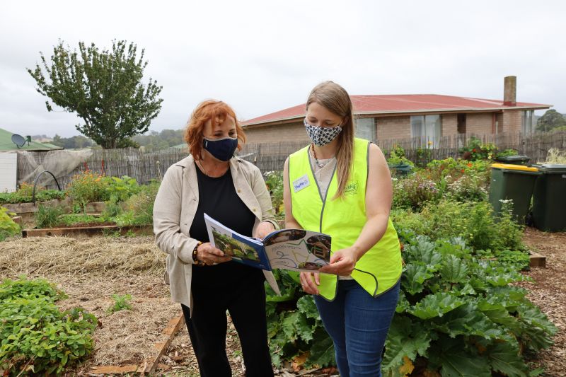 Two people stand in the Burnie Community House Garden reading the new Healthy Tasmania Five-Year Strategic Plan together. 